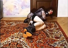 Crossdresser in armbinder, with gag and bootie cork lies on the floor corded up