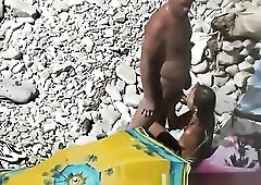 Nudist woman siting in the rocky beach blows her standing stud's dick.