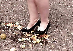 Older big beautiful woman stomps apples outdoors. Chubby legs in short jeans shorts and ebony patent leather shoes walk on those fruits, ruthlessly cr