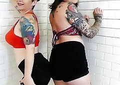 2 light-skinned brunettes in red lace underware pose back-to-back, seated, bent over, and on all fours, grabbing and widening every other’s exposed 