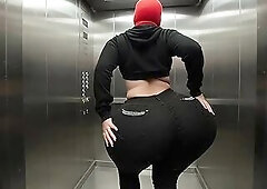 A voluptuous woman with an extremely massive booty is dancing softly inside the elevator wearing taut ebony jeans. The camera stays behind her capturi