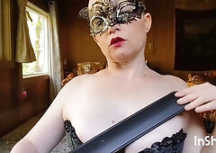 Strict dominatrix in black corset and mask disciplines with paddle and flogger