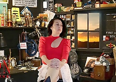 Light-skinned figure in floral skirt teases upskirt view in cluttered workshop under hypnotic influence
