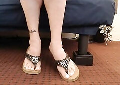Anna's feet in flip flops. White toenails, toe wiggling and pointing in leather guess sandals. Sitting and brief standing.
