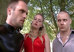Domme in red dominates two male slaves in latex during a forest walk